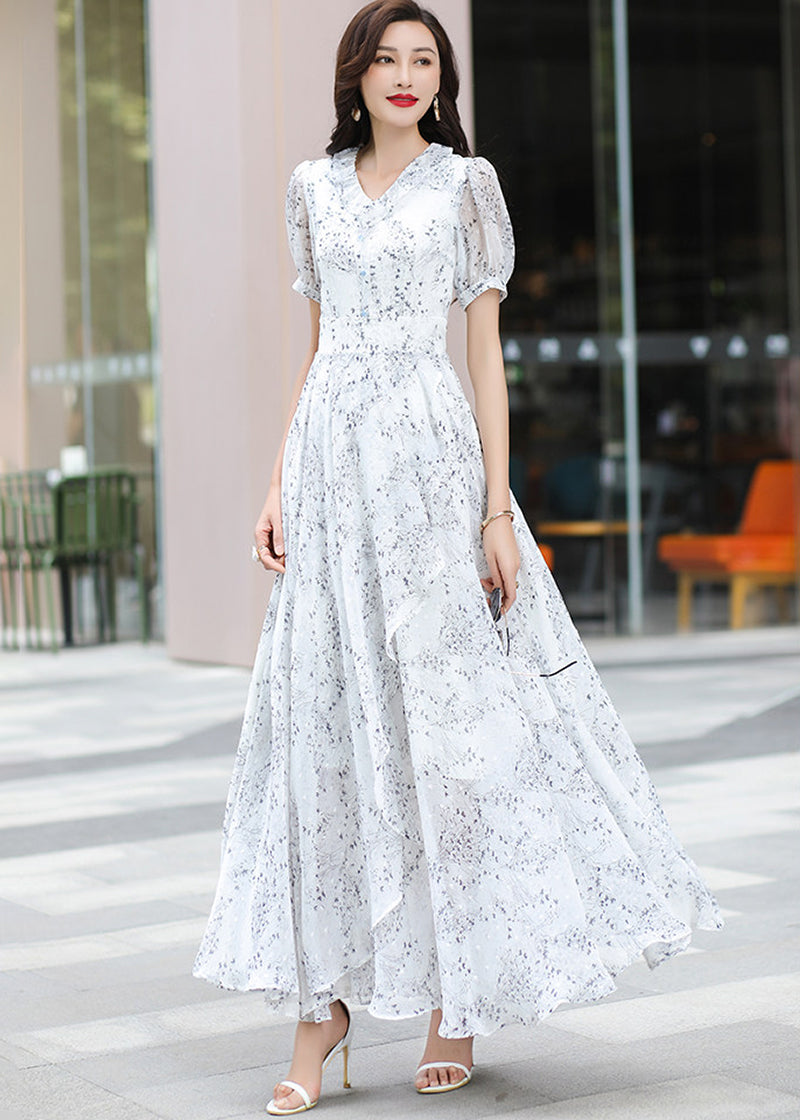 Dynamic full-length shot of a woman in motion, showing the wide, swirling skirt of the Vivian Seven chiffon maxi dress as she turns. She is wearing sunglasses and white sandals on a modern tiled walkway.