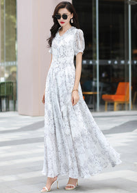 A lovely full-length shot from a slight angle of a woman in a long-sleeved floral maxi dress from Vivian Seven, holding sunglasses. The light floral print on white chiffon looks airy and perfect for spring.