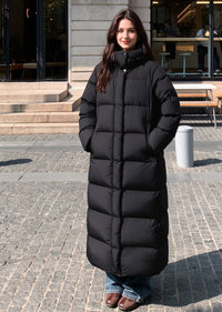 Full length front view of smiling woman with hands in pockets wearing black 50 inches long stand collar down puffer coat