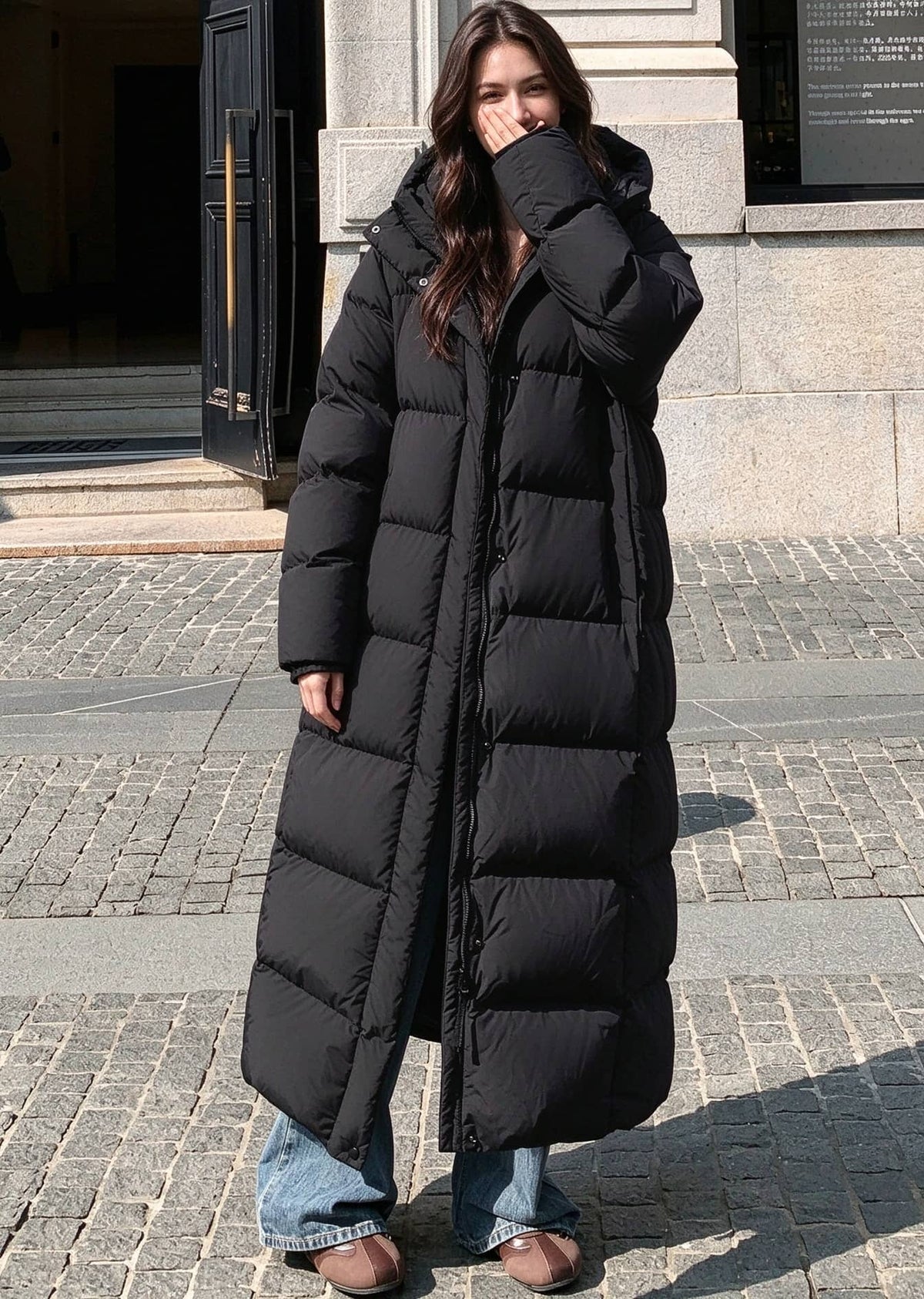 Full length front view of woman wearing open black 50 inches length hooded duck down puffer coat outdoors
