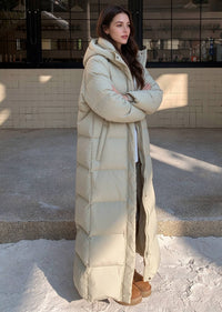 Full length side view of woman with arms crossed wearing beige 50 inches length stand collar down puffer coat