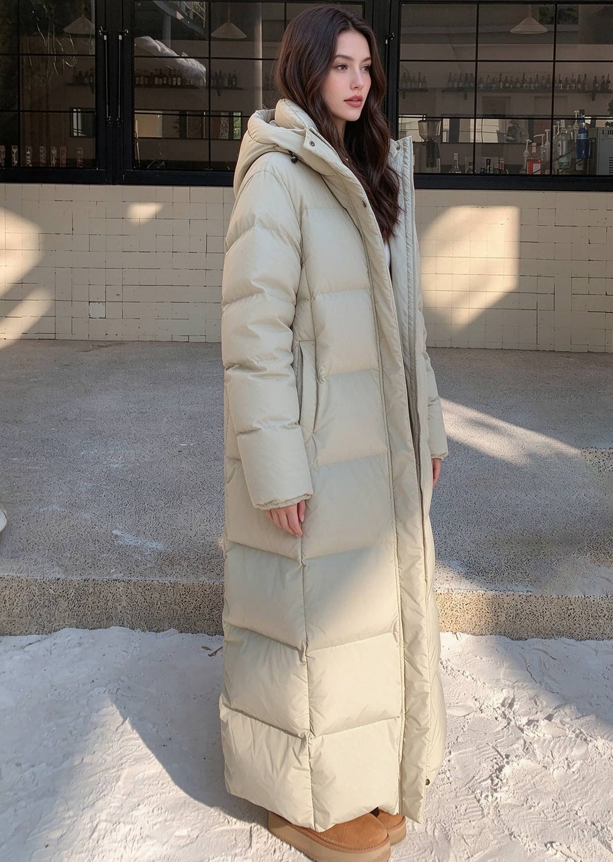 Three-quarter side shot of woman wearing beige 50 inches long hooded duck down puffer coat