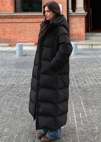 Three-quarter side view of woman with hand in pocket wearing black 50 inches long down puffer coat