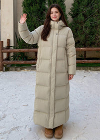 Full length front view of smiling woman waving hand wearing beige 50 inches long stand collar down puffer coat