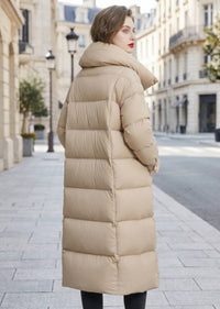 Side back view of woman wearing beige quilted longline down puffer coat with high collar