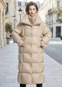 Front view of woman wearing buttoned beige double collar longline down coat with hands in pockets