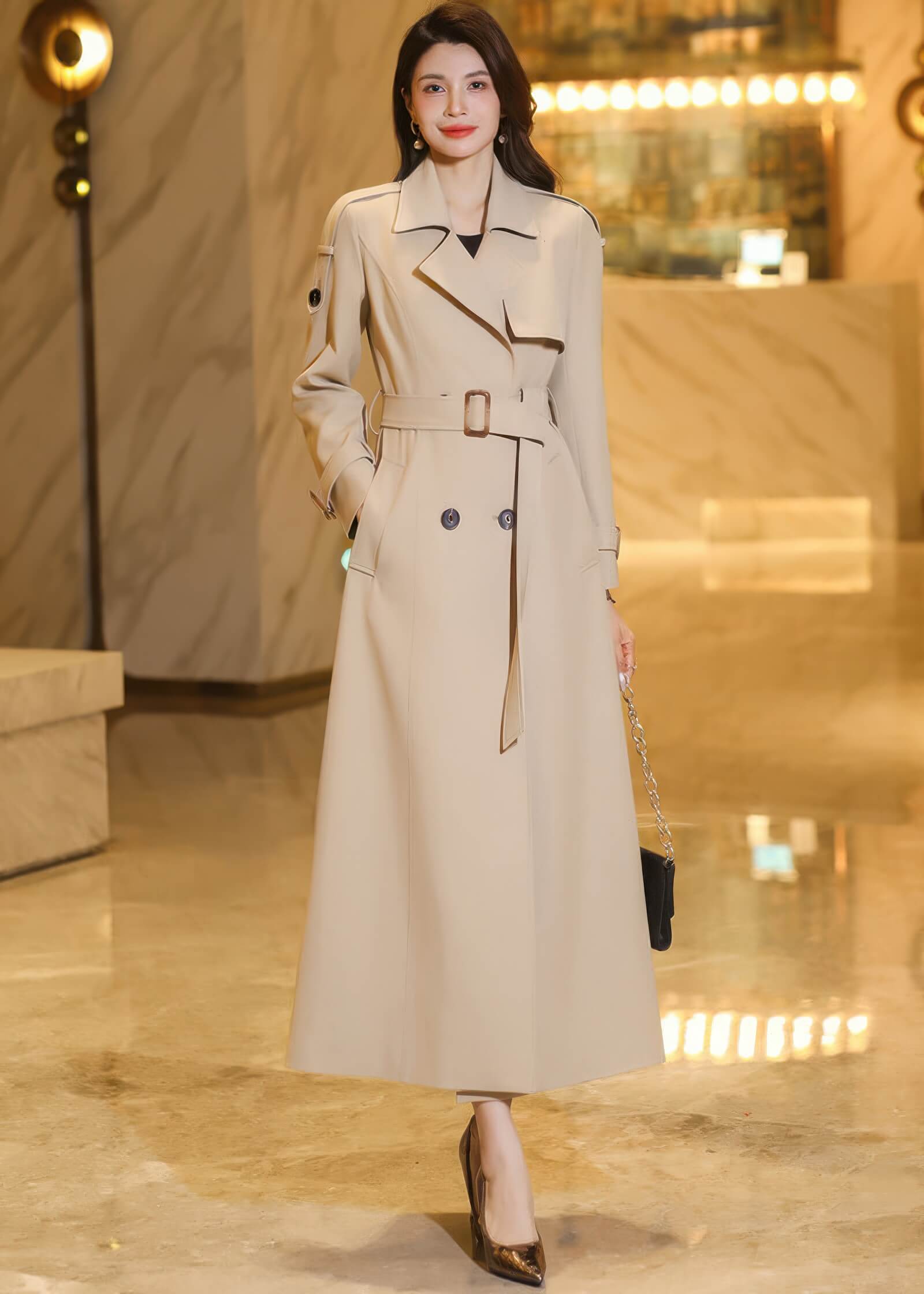 Elegant pose featuring a belted maxi khaki trench coat with a focus on the classic buckle and lapel details.