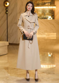 Front view of a belted long khaki trench coat featuring structured shoulders and buttoned cuff details.