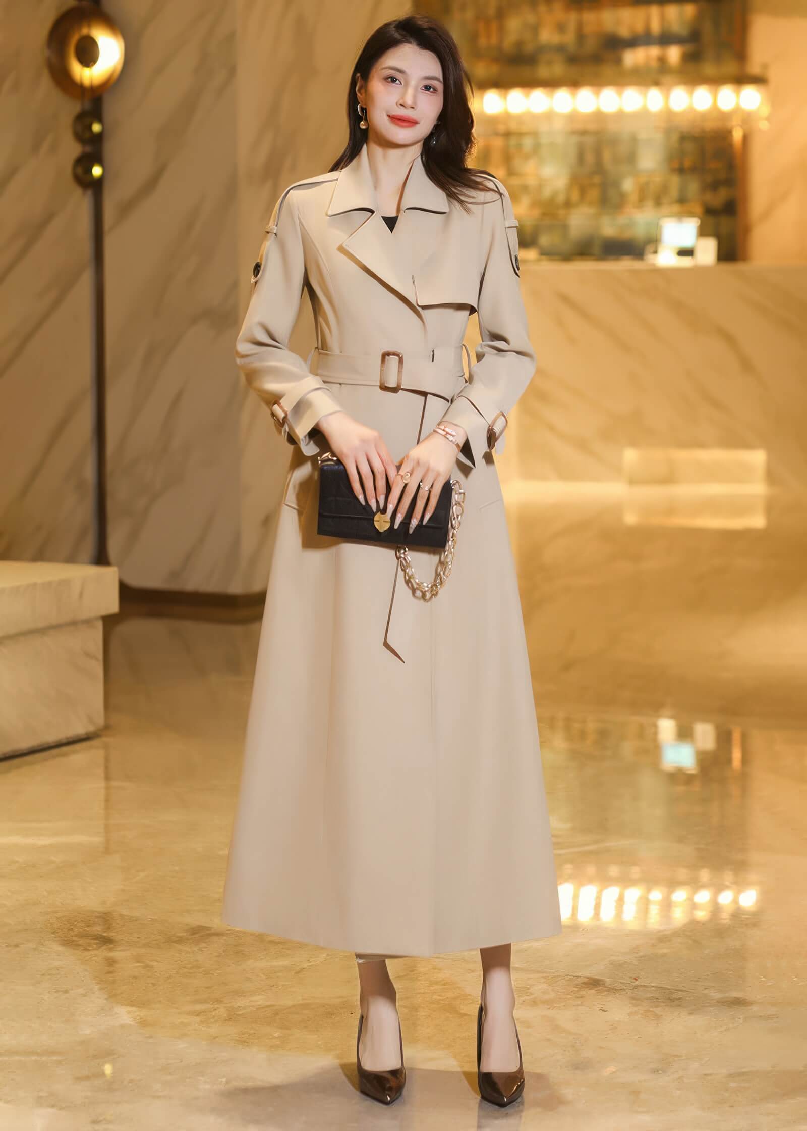 Front view of a belted long khaki trench coat featuring structured shoulders and buttoned cuff details.
