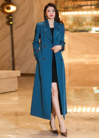 Woman wearing an open teal blue long trench coat over a black mini dress with hands in pockets.