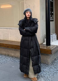 Front view of woman wearing long black duck down puffer coat with waist tie belt and grey beret.