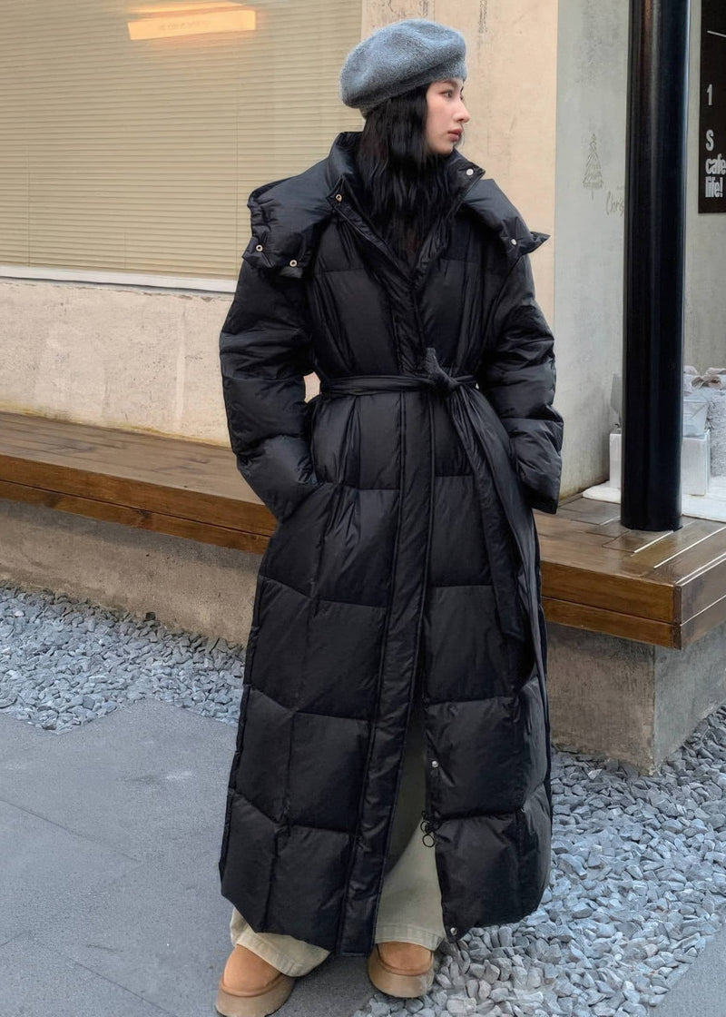 Full-length shot of woman wearing belted black duck down puffer longline coat with neutral winter outfit.