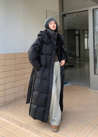 Full-length view of woman wearing open black hooded duck down maxi puffer coat with wide-leg pants.