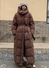 Full-length women's warm brown hooded duck down puffer coat with tied sash belt and ribbed beanie.