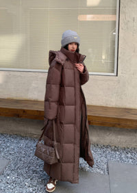 Front-three-quarter view of brown maxi winter down coat with stand collar, hood, and quilted purse.