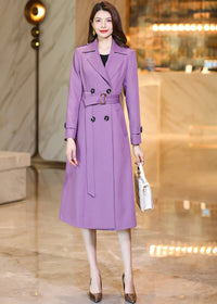 Model posing in a Vivian Seven purple long trench coat holding a small white designer handbag.