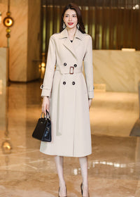 Vivian Seven beige double-breasted long trench coat paired with a black structured handbag and metallic pumps.