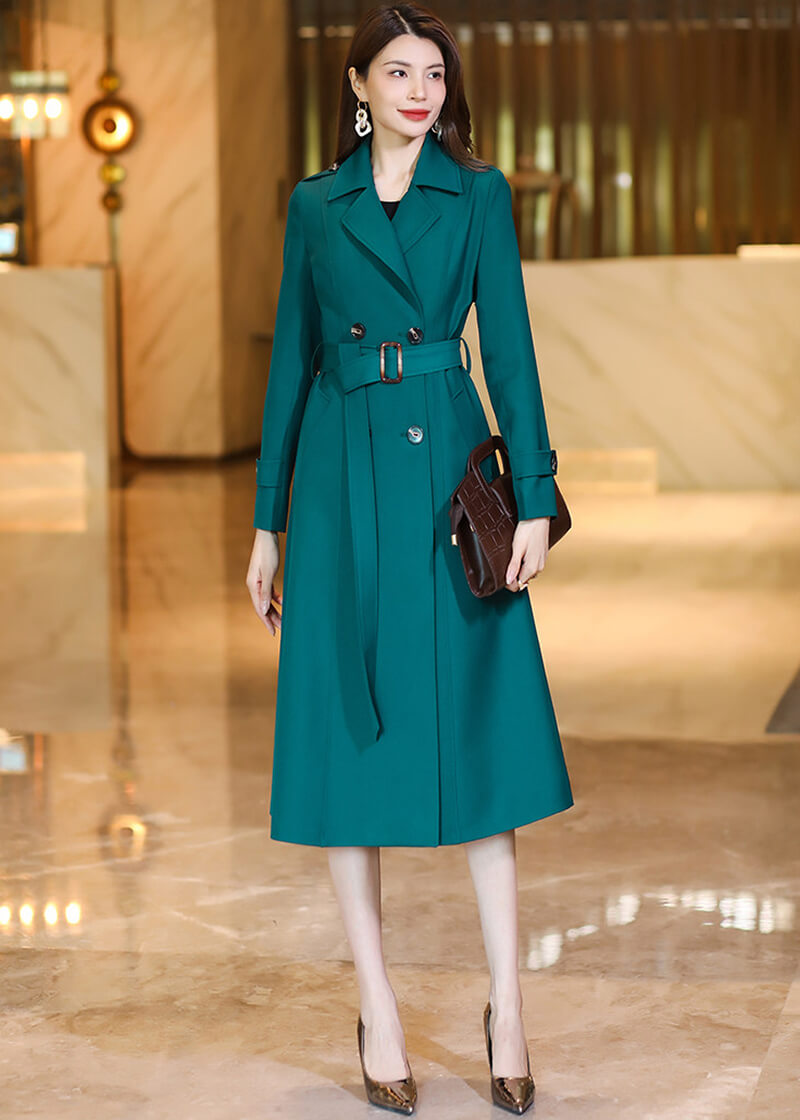 Model wearing the Vivian Seven dark teal trench coat styled with a matching belt and a brown textured leather handbag.