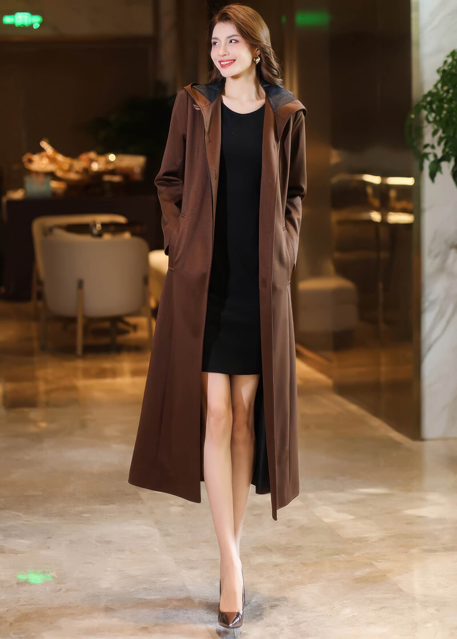 Full-length shot of an open brown hooded trench coat showcasing the dark interior lining and a minimalist silhouette.