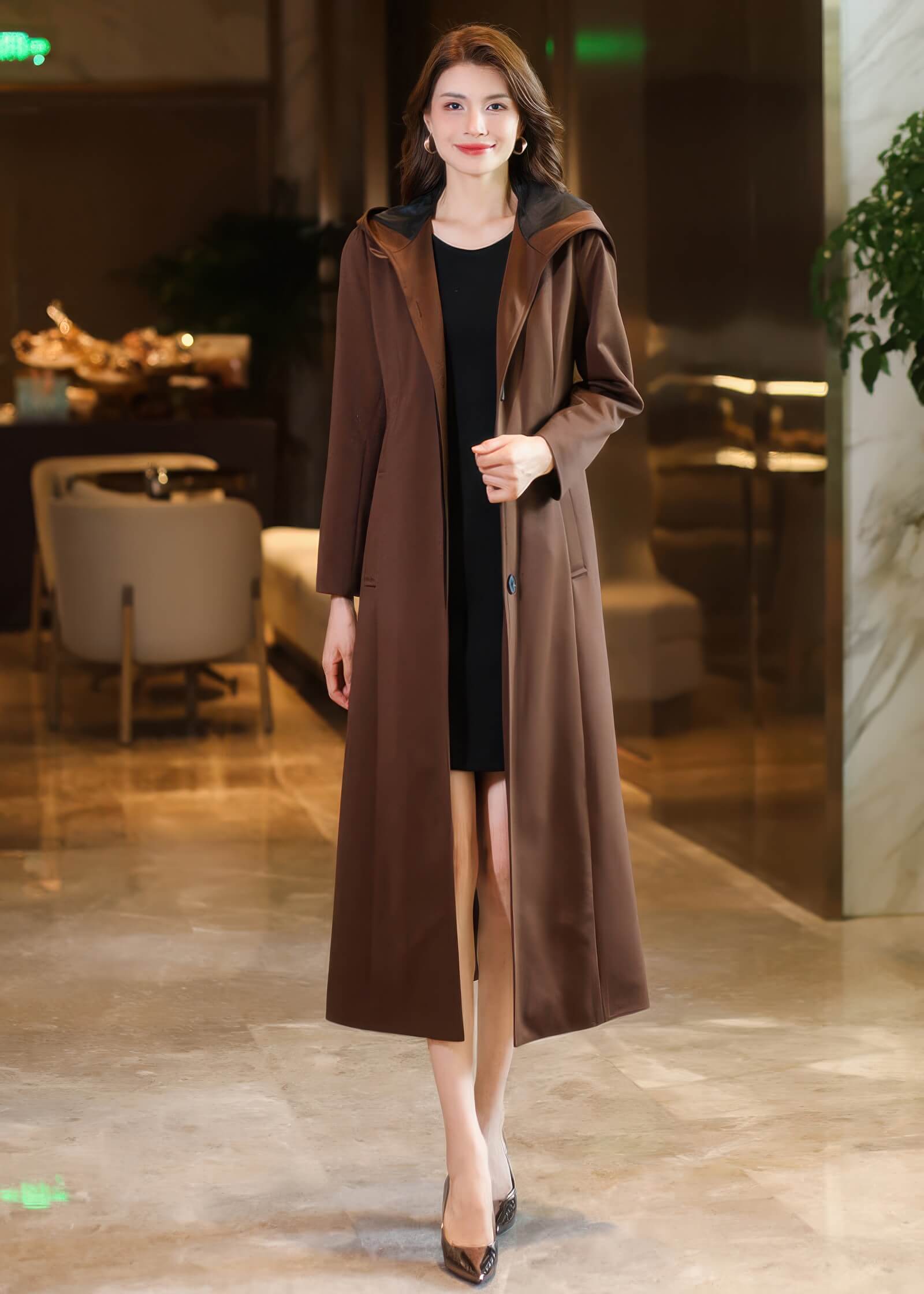 Frontal view of a tailored women's long brown coat with a hood and single-button closure, styled for a professional look.