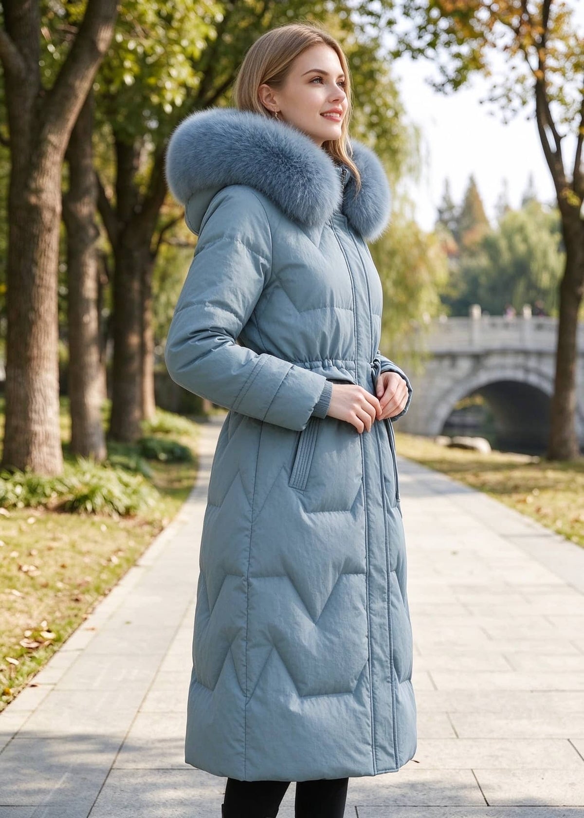Three-quarter side view of woman posing outdoors in dusty blue genuine sheepskin leather down coat with drawstring waist