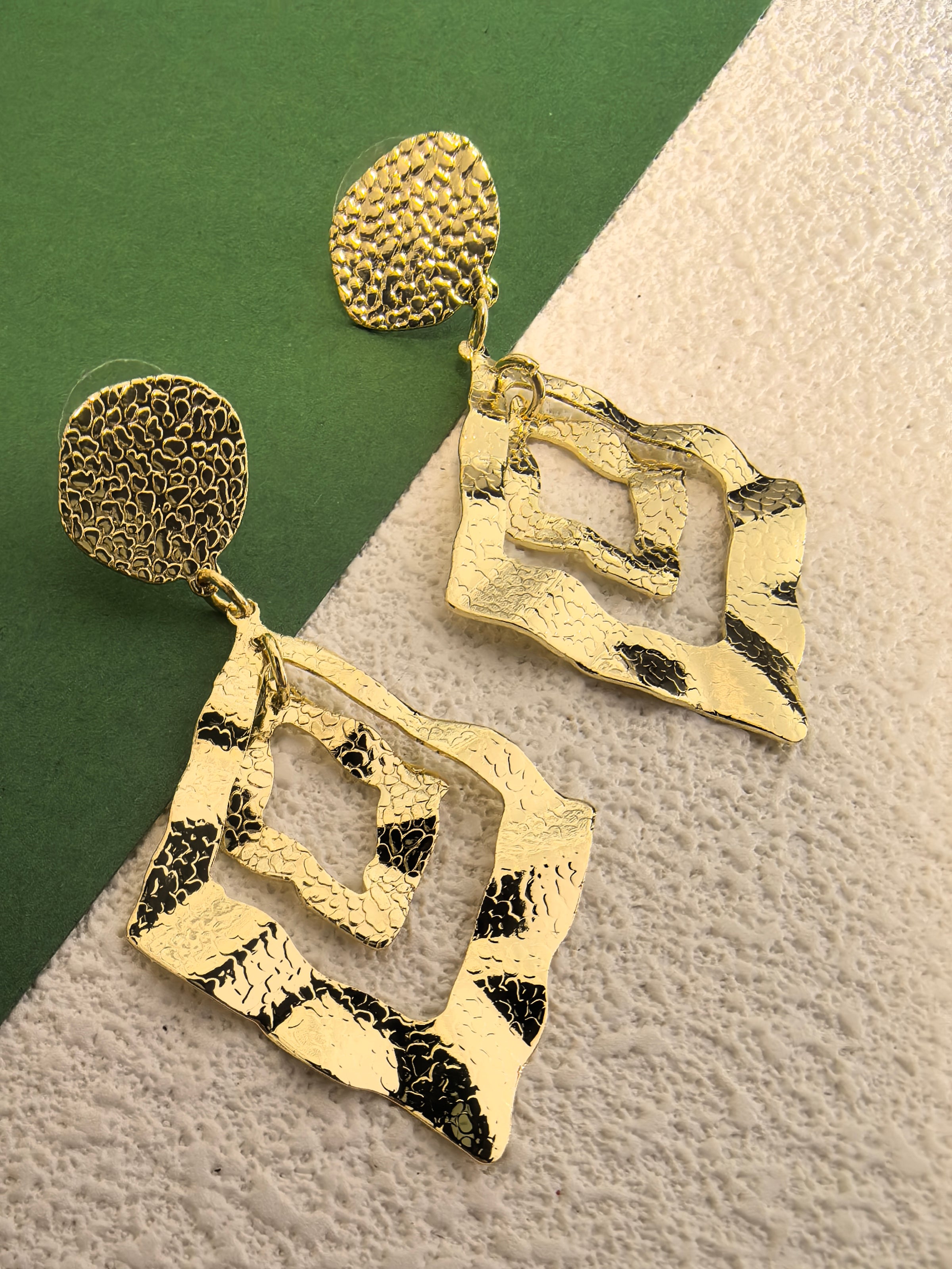 Extreme close-up of the hammered metal texture on the gold geometric earrings, highlighting the intricate, light-catching indentations.