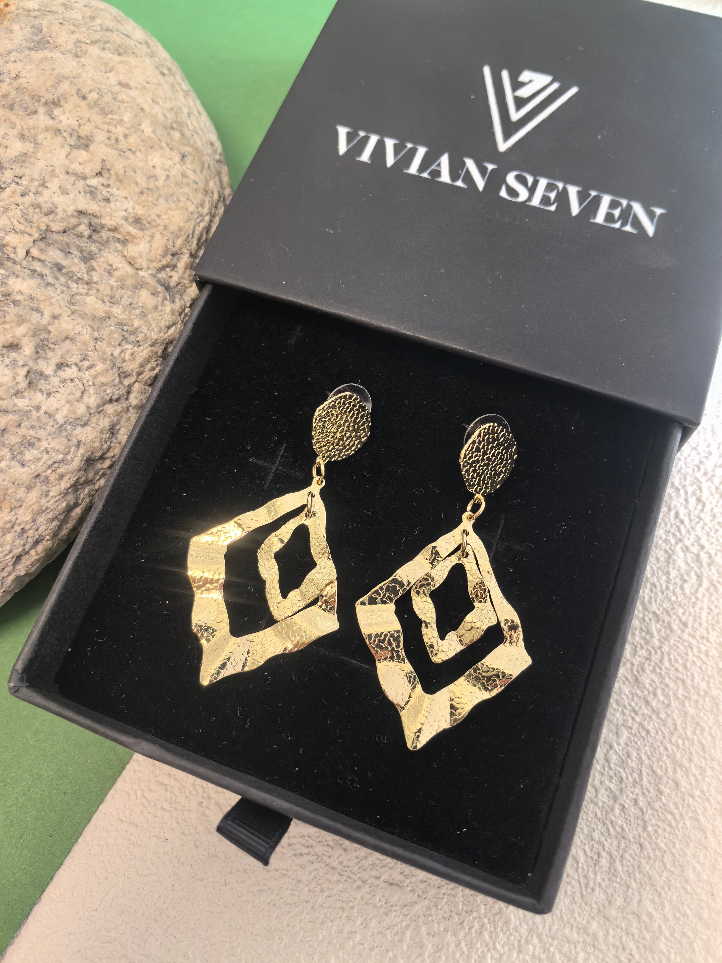 Pair of textured gold diamond-shaped earrings nestled inside a black velvet-lined "Vivian Seven" jewelry box.