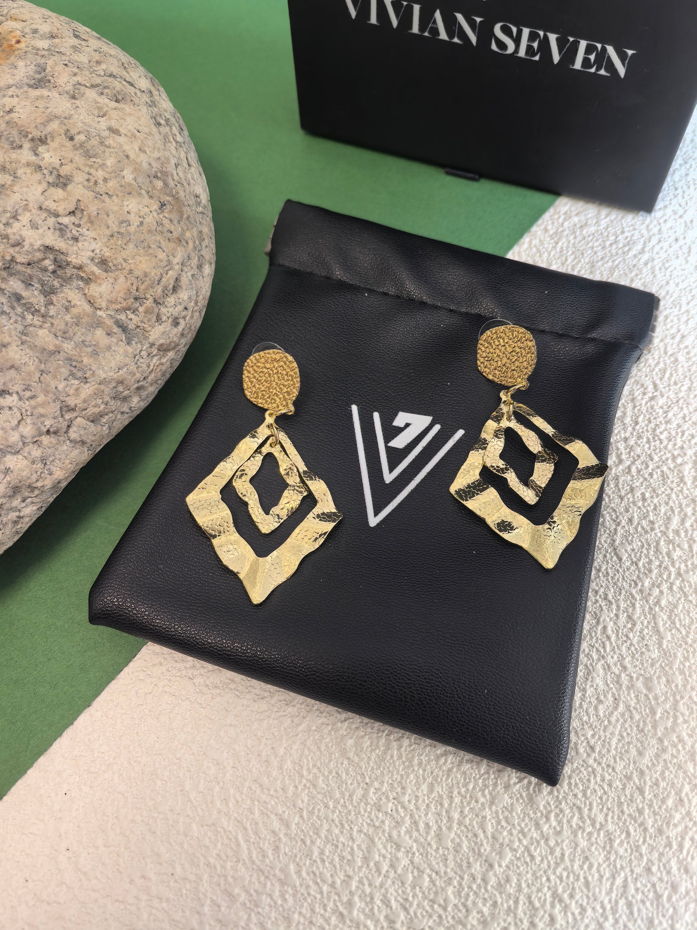 Gold hammered earrings resting on a black faux-leather jewelry pouch branded with a white "V7" logo.