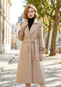 Front view of woman holding lapel wearing beige herringbone wool cashmere coat with tied belt