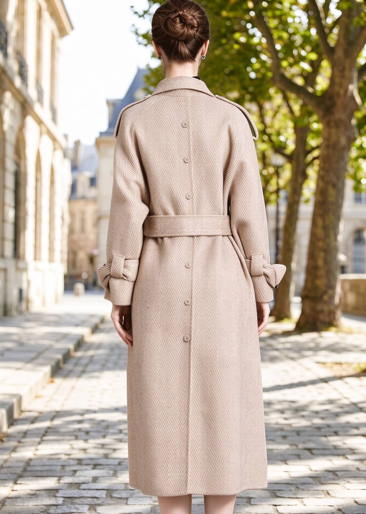 Back view of woman wearing beige herringbone wool coat featuring belted waist and buttoned back seam