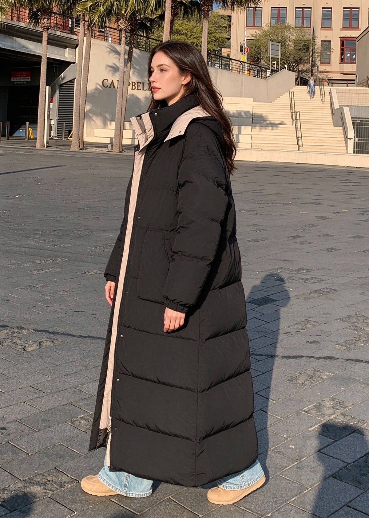 Full length side view of woman walking in black longline puffer parka with contrast beige hood lining