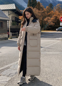 Full length front view of woman walking outdoors in beige hooded longline puffer parka with cargo flap pockets