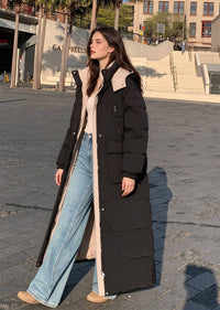 Three-quarter front view of woman wearing open black hooded longline puffer parka with cargo pockets