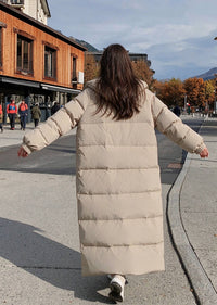 Full length back view of woman with arms outstretched wearing beige hooded longline polyfill puffer parka