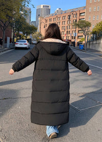 Full length back view of woman with arms open wearing black hooded longline puffer parka in city street