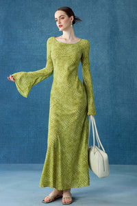 A woman posing in a lime green swirl-patterned maxi dress with flared bell sleeves and a scoop neckline. She is holding a large cream-colored leather handbag and looking to the side.