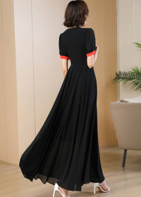 A rear view of the woman looking back over her shoulder, showcasing the back design of the black chiffon maxi dress. The clean lines of the A-line silhouette and the pop of red color on the short sleeve cuffs are visible from behind.