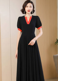 A medium close-up shot focusing on the upper half of the black chiffon dress. The detail of the structured, bright red V-neck collar and matching sleeve cuffs is clearly visible. The woman has short, styled dark hair and is wearing elegant drop earrings.