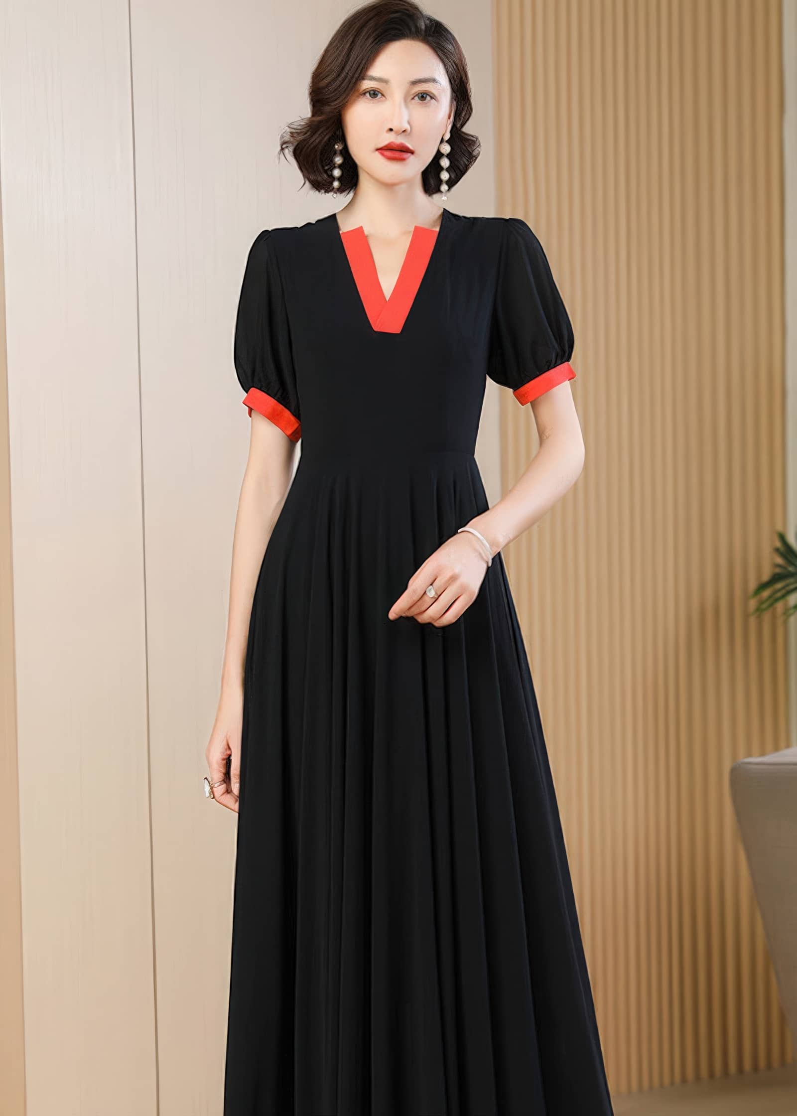 A medium close-up shot focusing on the upper half of the black chiffon dress. The detail of the structured, bright red V-neck collar and matching sleeve cuffs is clearly visible. The woman has short, styled dark hair and is wearing elegant drop earrings.