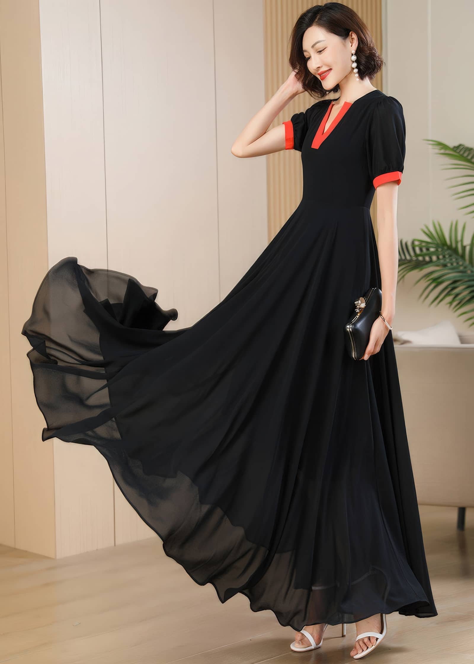 A dynamic side-angle shot of the woman holding a small black evening clutch. The black chiffon skirt of the maxi dress is captured mid-swing, revealing the sheer, lightweight quality of the layered fabric.