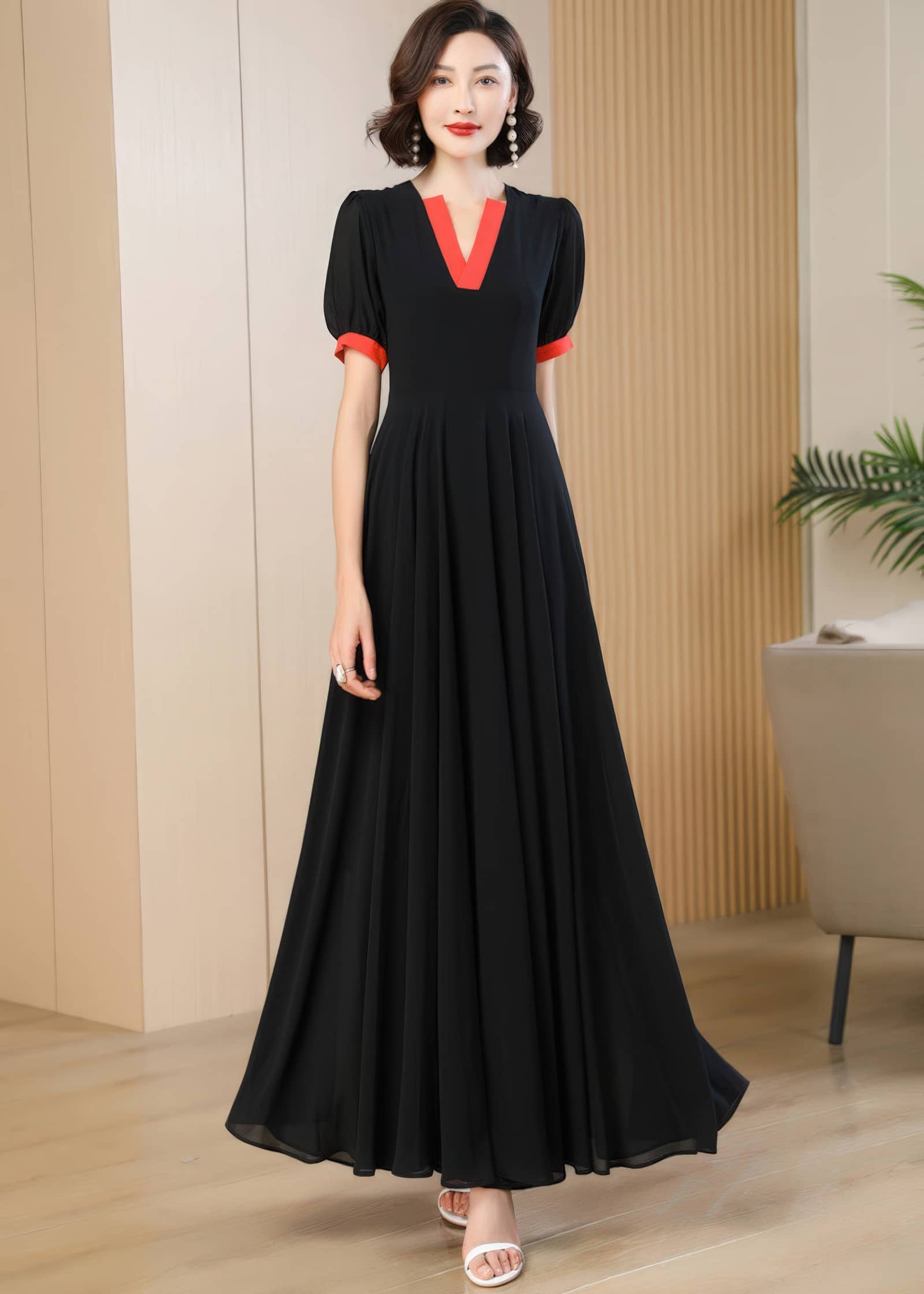 A straight-on, full-body studio shot of the woman wearing the contrast black and red-orange chiffon A-line dress. The pleats at the waistline of the skirt fall cleanly to the floor, presenting a formal and balanced look.
