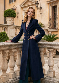 Three-quarter view of woman leaning on stone balustrade wearing navy blue corduroy fit and flare long overcoat