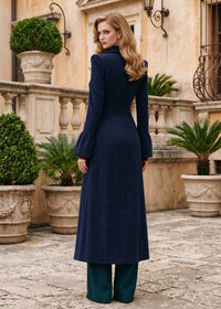 Three-quarter back view of woman wearing navy blue flared corduroy long coat showing bell cuffs and tailored waist