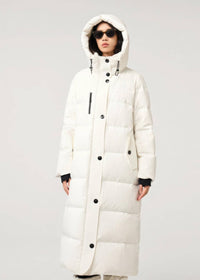 A model wearing a long, hooded puffer coat in off-white with black buttons and black ribbed cuffs, set against a plain light gray studio background.