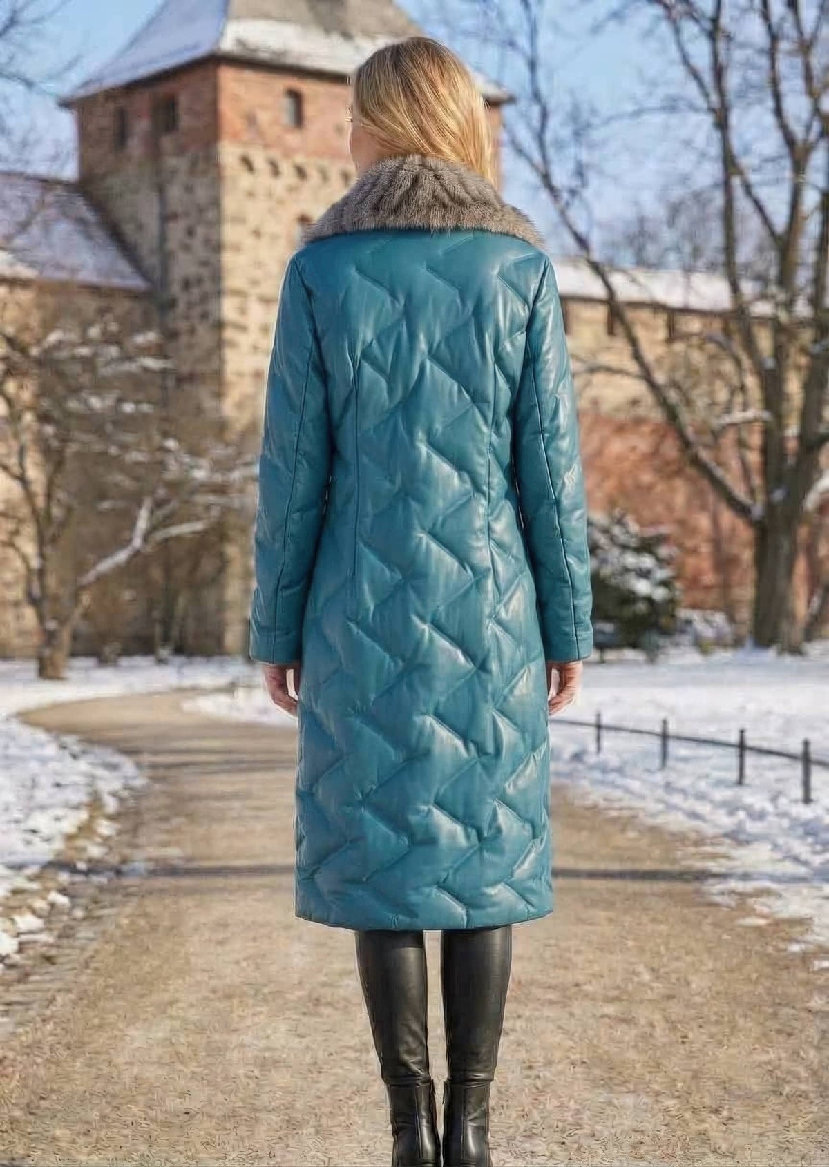 Full length back view of woman wearing teal blue quilted genuine sheepskin leather long down coat in snow background