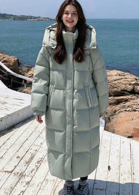 Full length front view of smiling woman standing outdoors wearing zipped sage green goose down puffer long coat