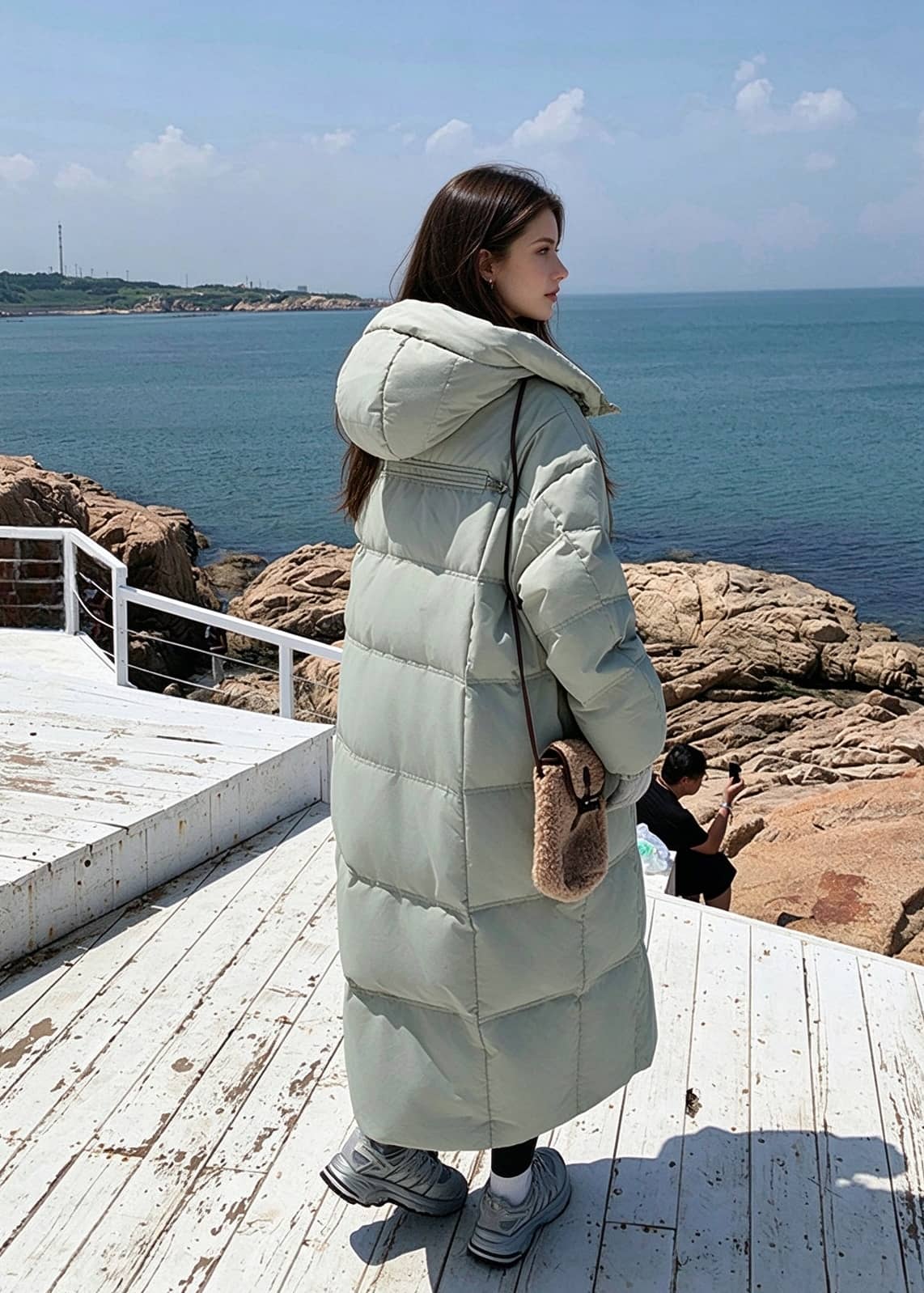 Back side profile view of woman wearing sage green quilted hooded long goose down puffer coat