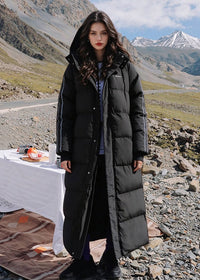 Full length front view of woman wearing black side-stripe longline puffer coat with detachable hood in mountainous area