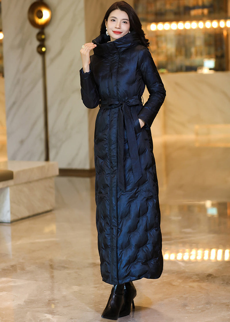 Full-length shot of a model wearing a belted midnight navy iridescent maxi down coat with hands in pockets