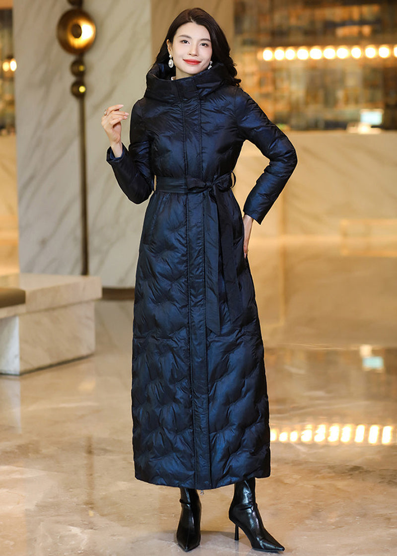 Full-length shot of a model wearing a belted midnight navy iridescent maxi down coat with hands in pockets
